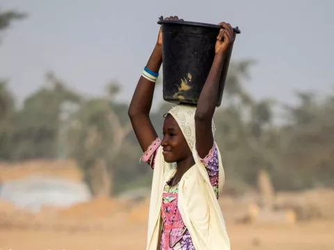 An adolescent girl carries a bucket of water