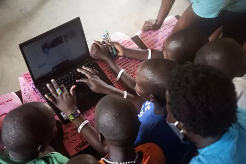 Children gather around a laptop